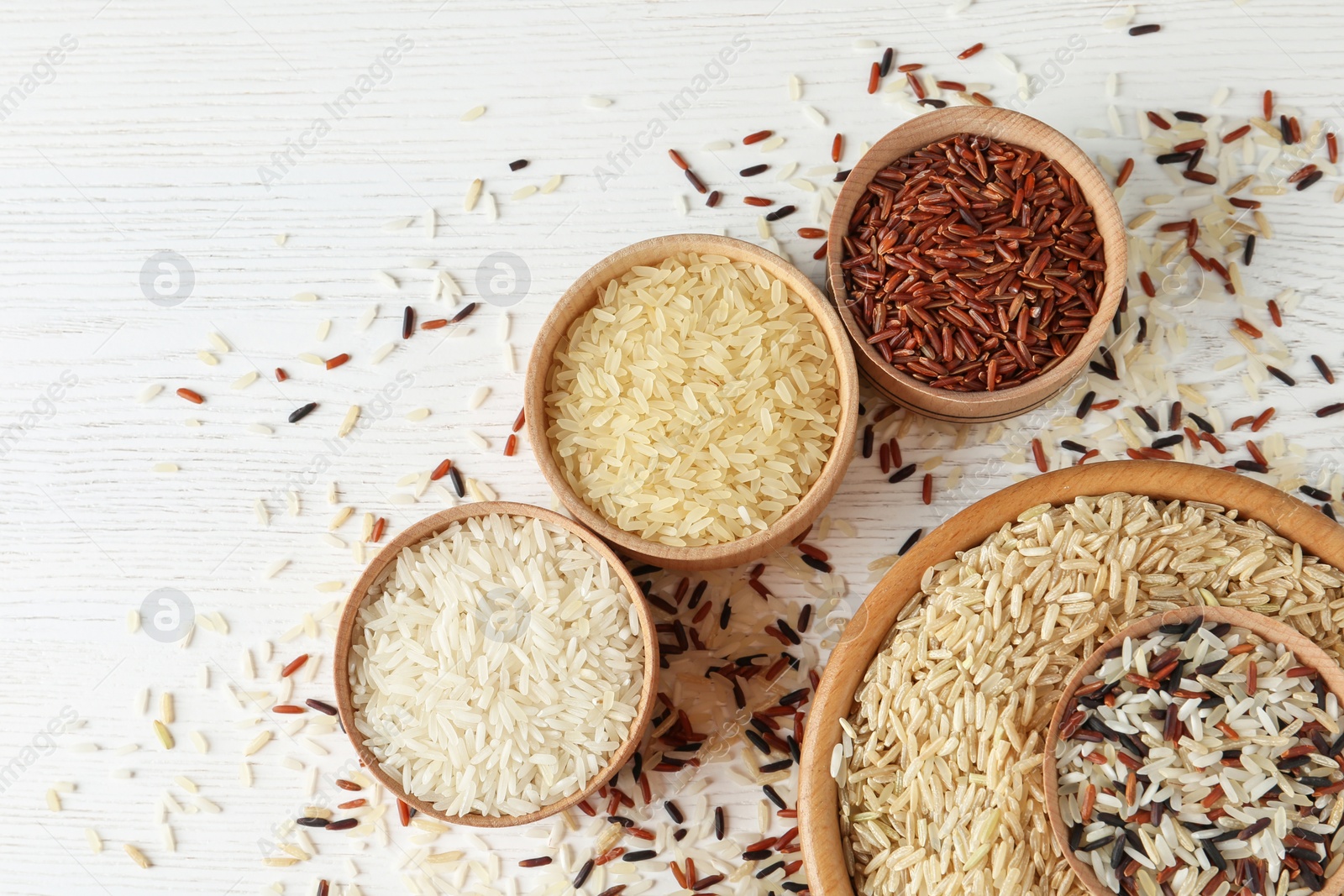 Photo of Flat lay composition with brown and other types of rice in bowls on white wooden background