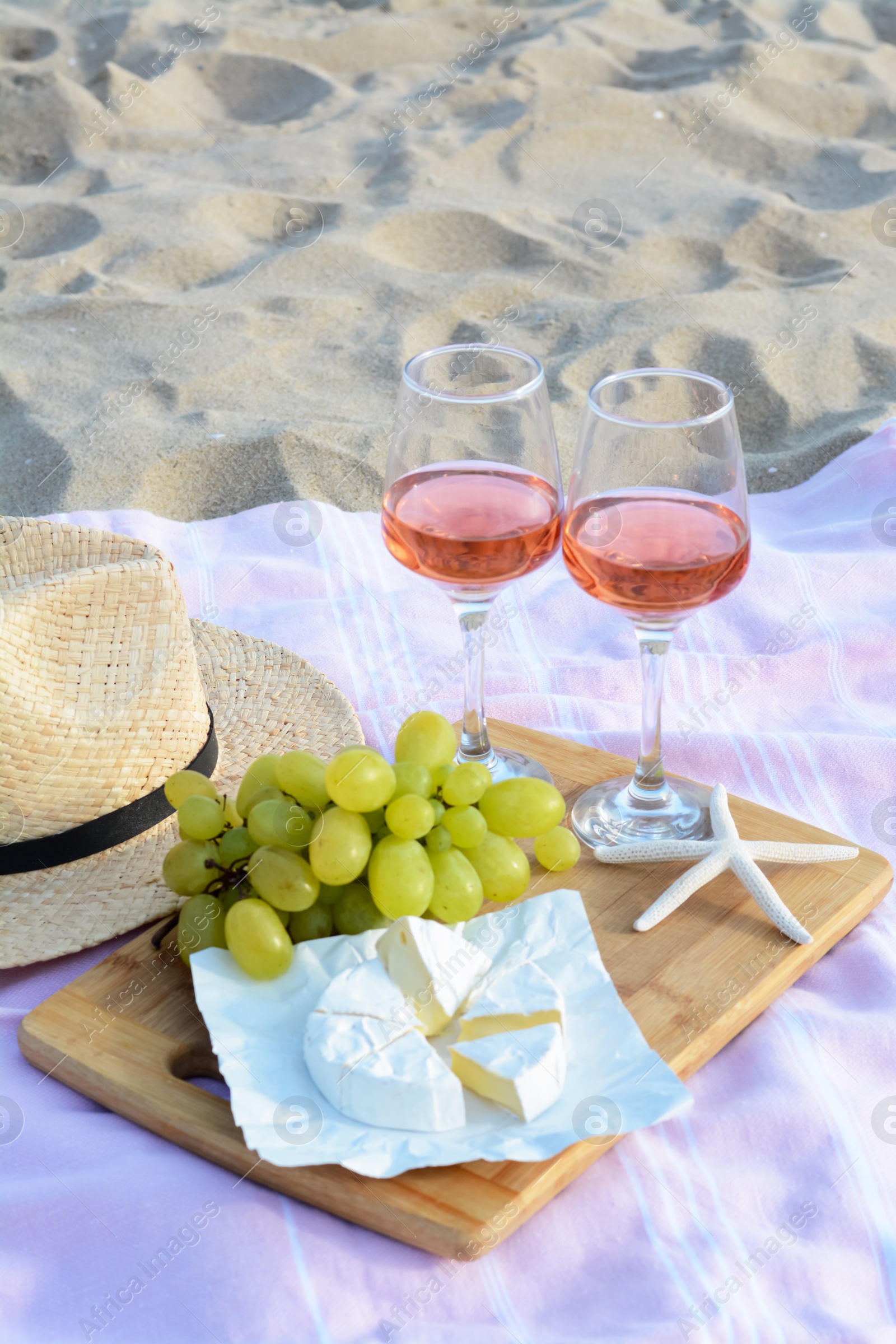 Photo of Glasses with rose wine and snacks for beach picnic on sand outdoors