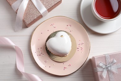 Photo of St. Valentine's Day. Delicious heart shaped cake, tea and gift on white wooden table, flat lay