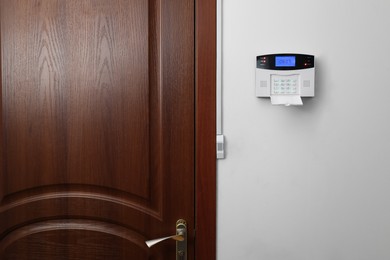 Photo of Home security alarm system on white wall near door, space for text