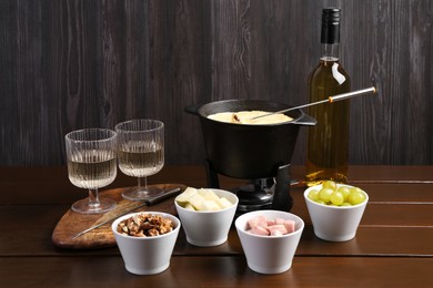 Fondue pot with tasty melted cheese, forks, wine and different snacks on wooden table