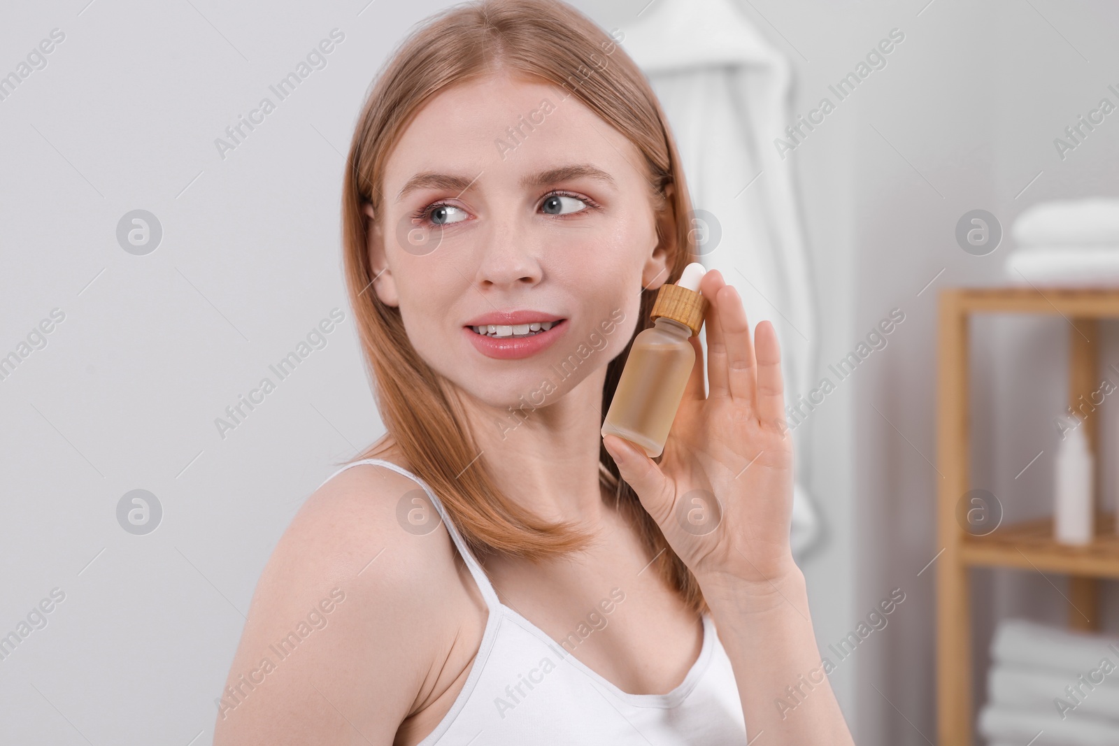 Photo of Young woman with bottle of essential oil in bathroom