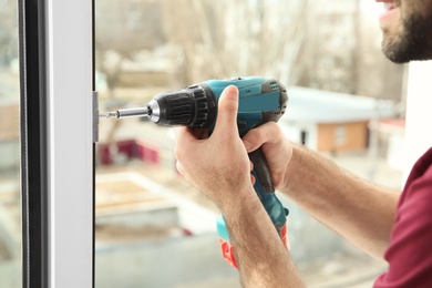 Construction worker using drill while installing window indoors, closeup
