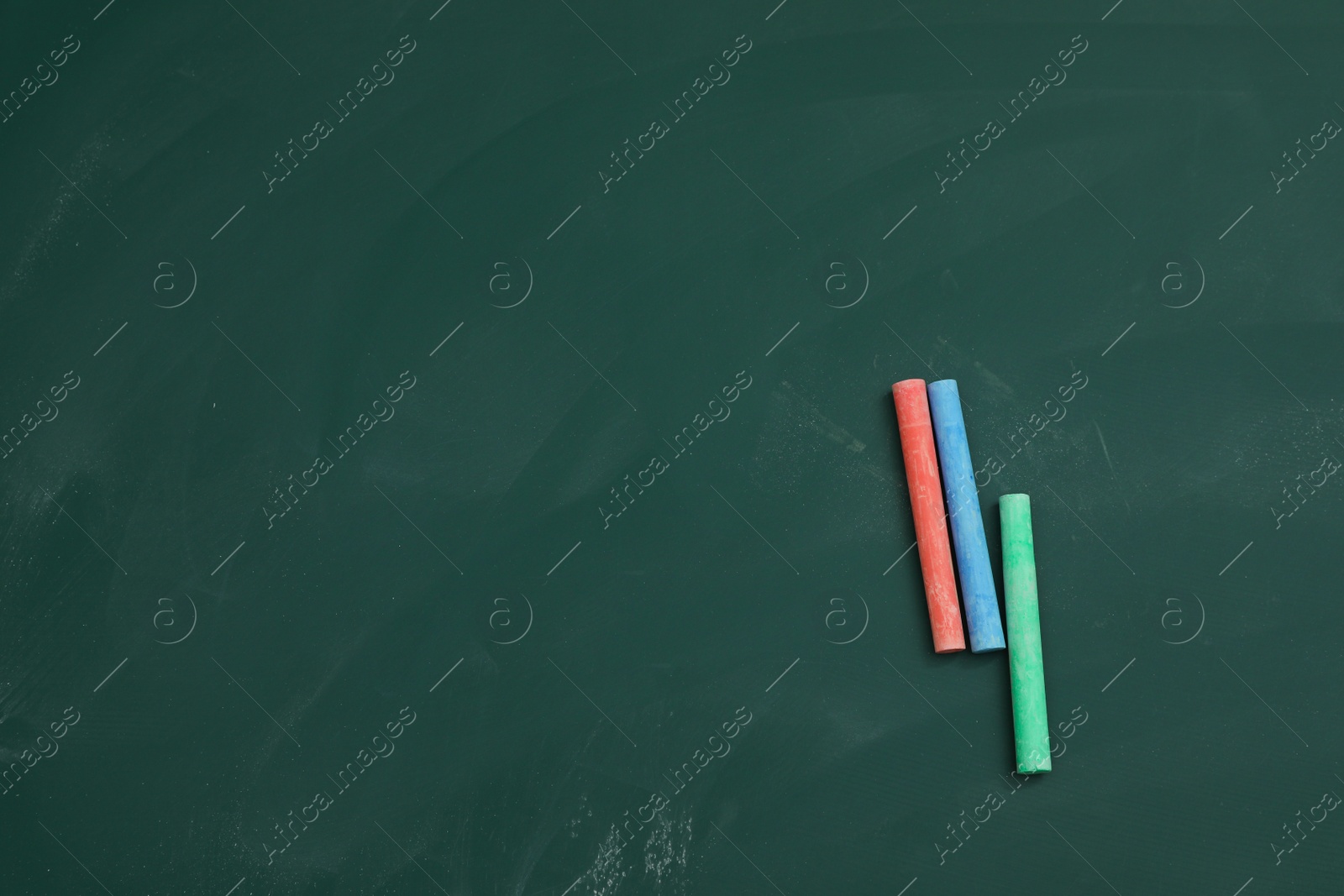 Photo of Colorful chalks on green board, flat lay. Space for text