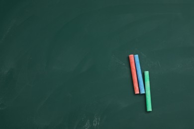 Colorful chalks on green board, flat lay. Space for text