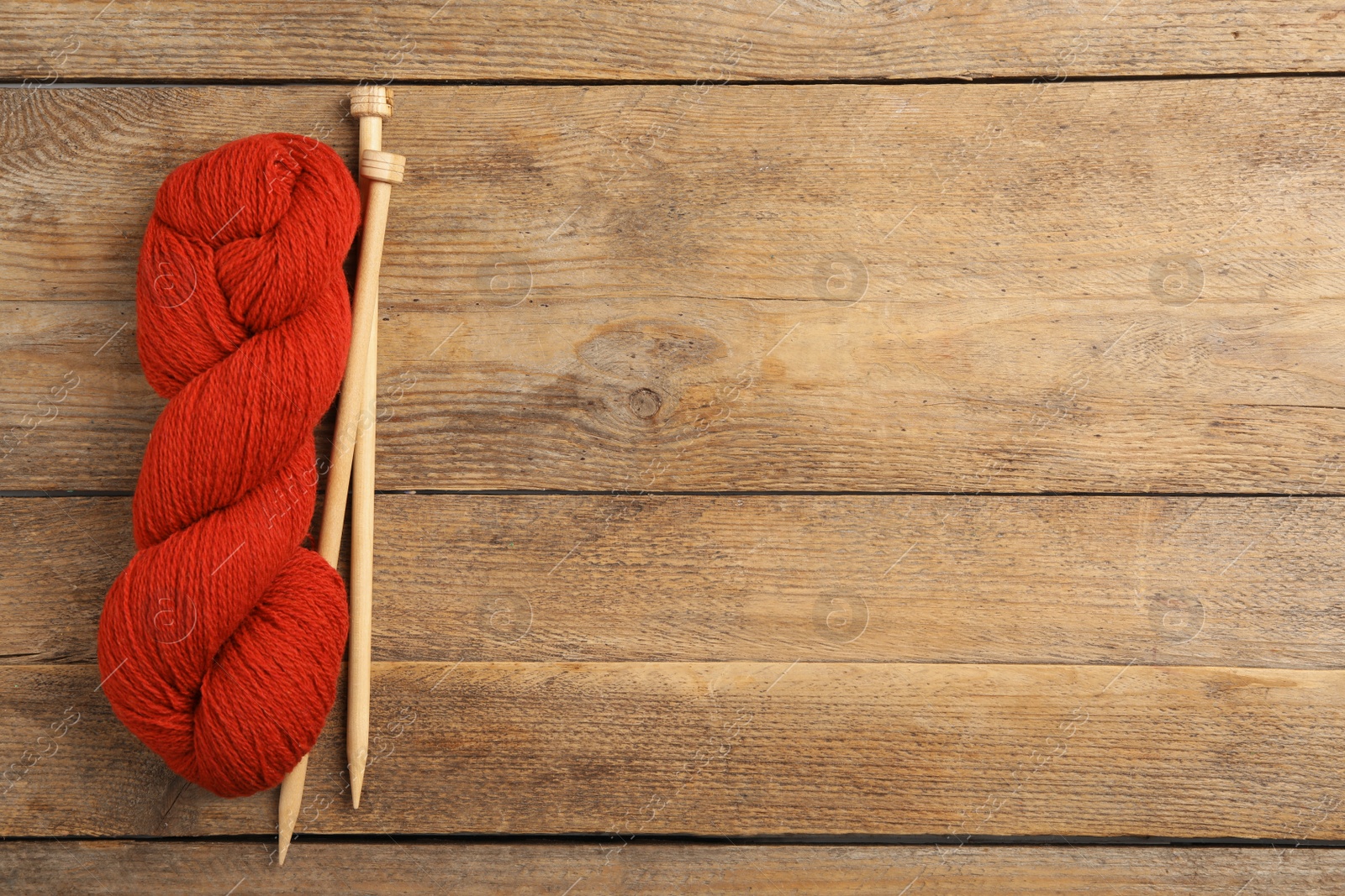 Photo of Soft red woolen yarn and knitting needles on wooden table, flat lay. Space for text