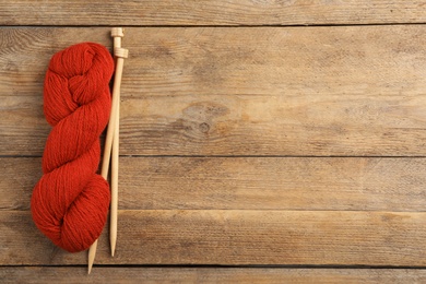 Soft red woolen yarn and knitting needles on wooden table, flat lay. Space for text