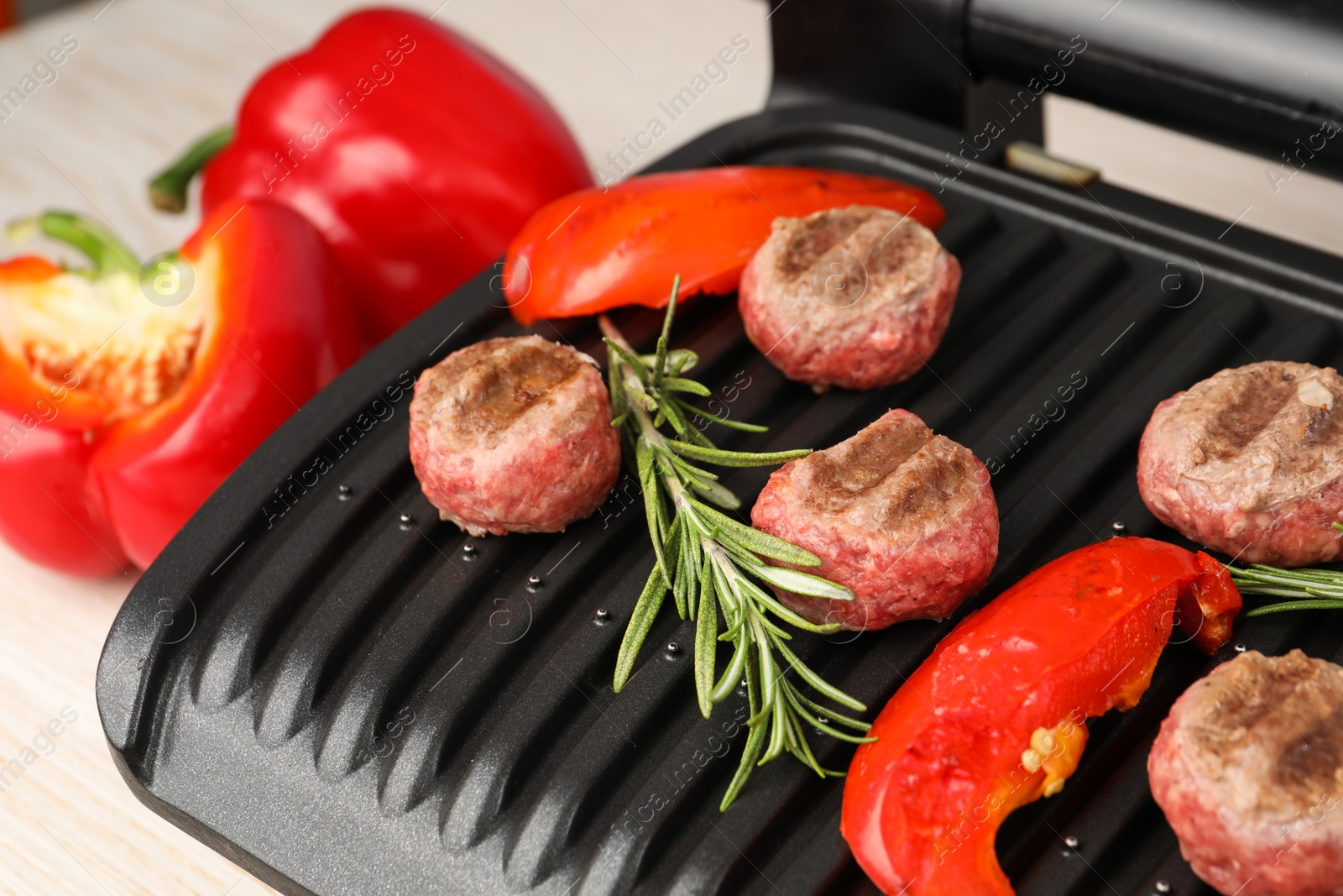 Photo of Electric grill with vegetables, meat balls and rosemary on table, closeup