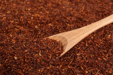 Photo of Heap of dry rooibos tea leaves with wooden spoon, closeup view