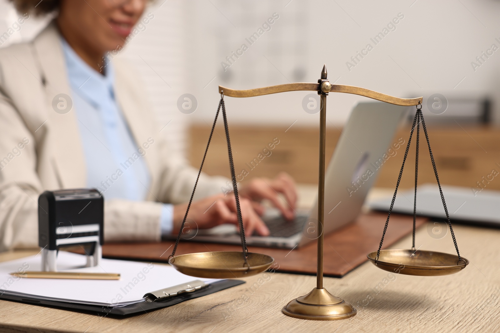 Photo of Notary using laptop at workplace in office, focus on scales of justice