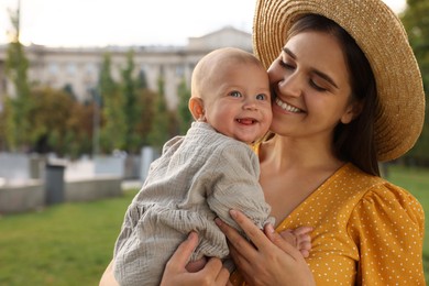 Happy mother with adorable baby walking in park on sunny day, space for text