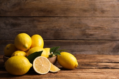 Many fresh ripe lemons with green leaves on wooden table, space for text