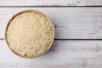 Photo of Raw rice in bowl on light wooden table, top view. Space for text
