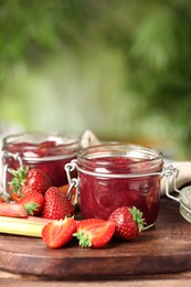 Tasty rhubarb jam in jars and strawberries on wooden table against blurred background. Space for text