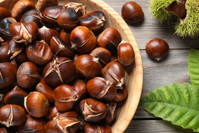 Photo of Delicious roasted edible chestnuts on brown wooden table, flat lay