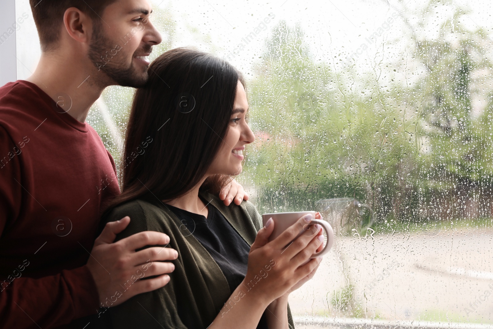 Photo of Happy young couple near window indoors on rainy day