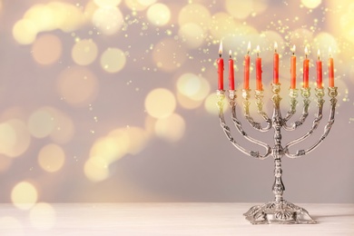 Image of Silver menorah with burning candles on table against light background, space for text. Hanukkah celebration