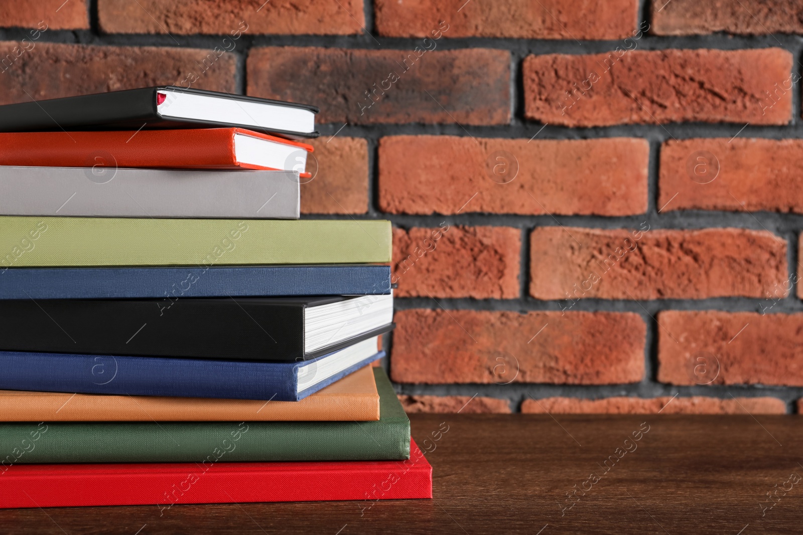 Photo of Stack of hardcover books on wooden table near brick wall. Space for text