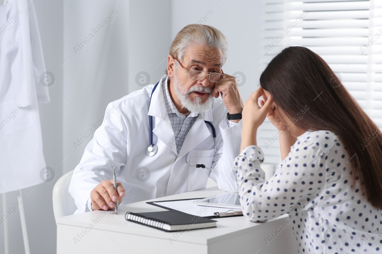 Photo of Senior doctor consulting patient at white table in clinic