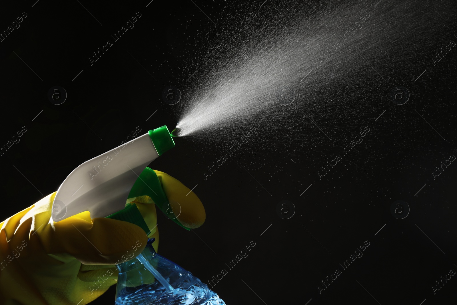 Photo of Woman spraying liquid from bottle on black background, closeup