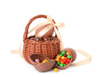 Wicker basket with tasty chocolate eggs and colorful candies on white background