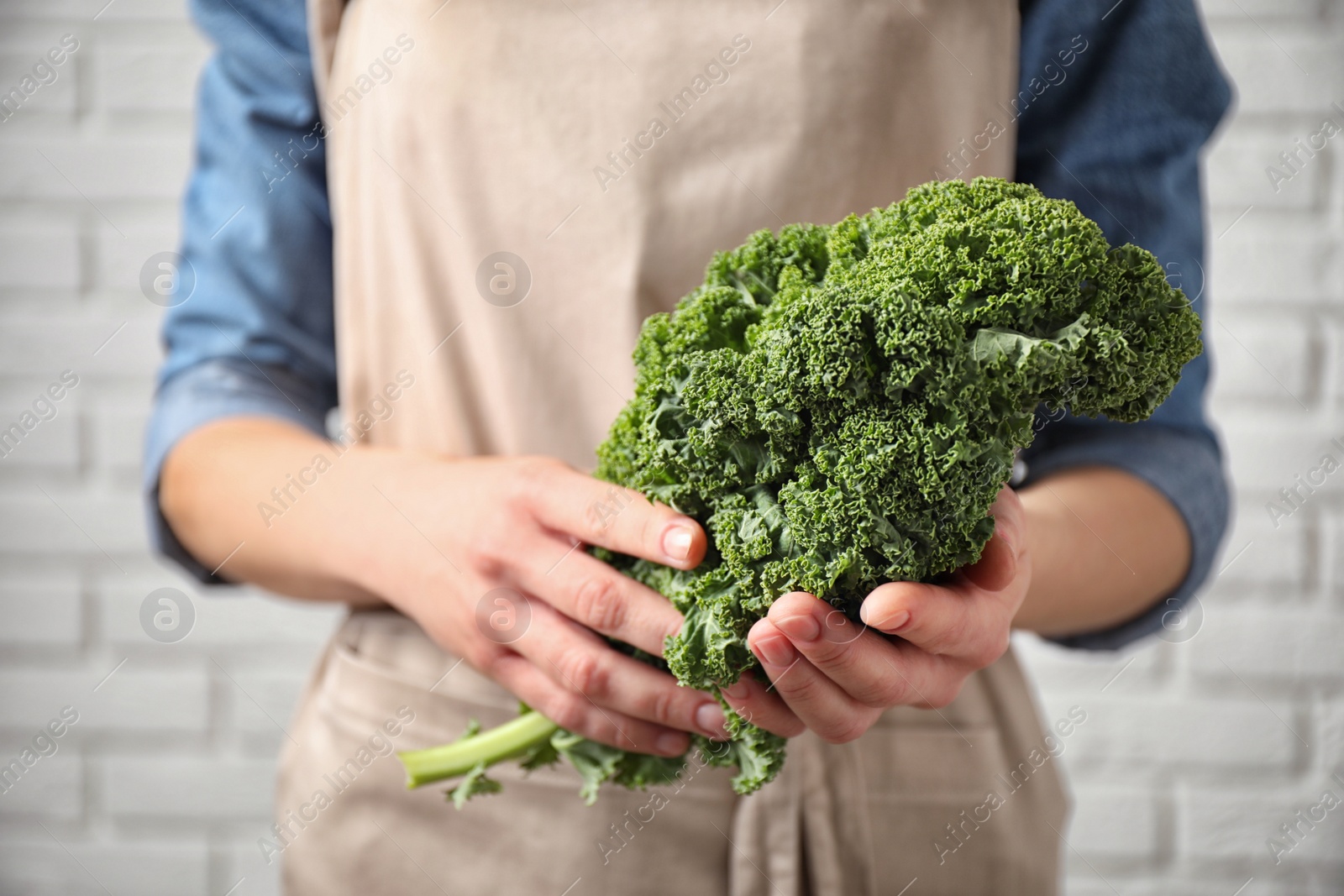 Photo of Woman holding fresh kale leaves near white brick wall, closeup