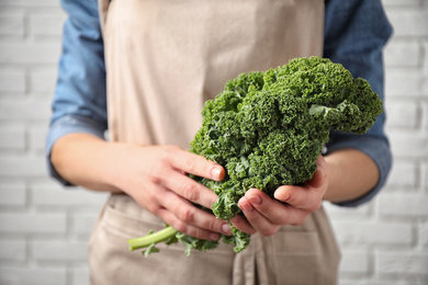 Photo of Woman holding fresh kale leaves near white brick wall, closeup