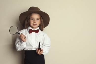 Cute little child in hat with smoking pipe and magnifying glass playing detective on beige background, space for text