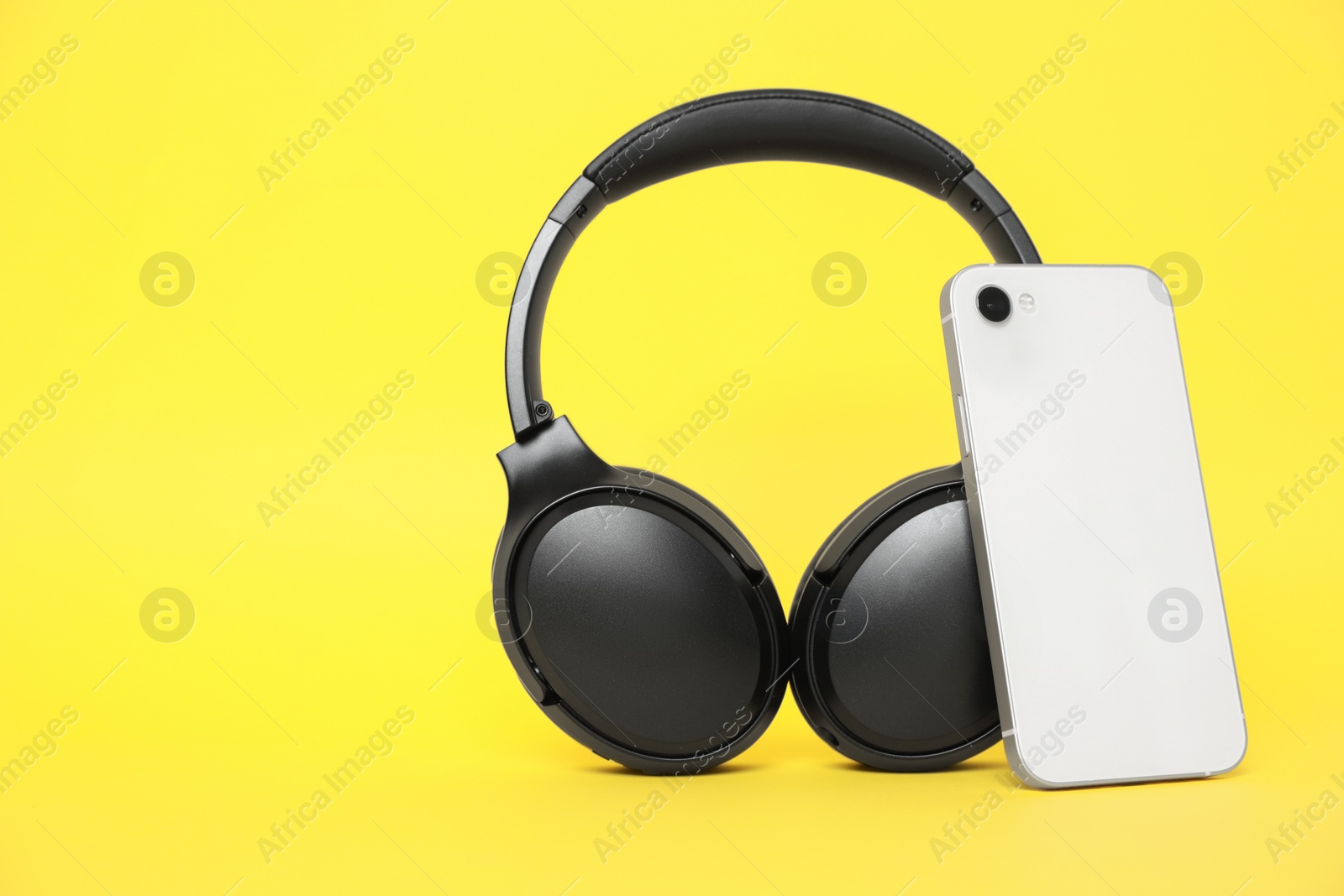 Photo of Modern wireless headphones and smartphone on yellow background