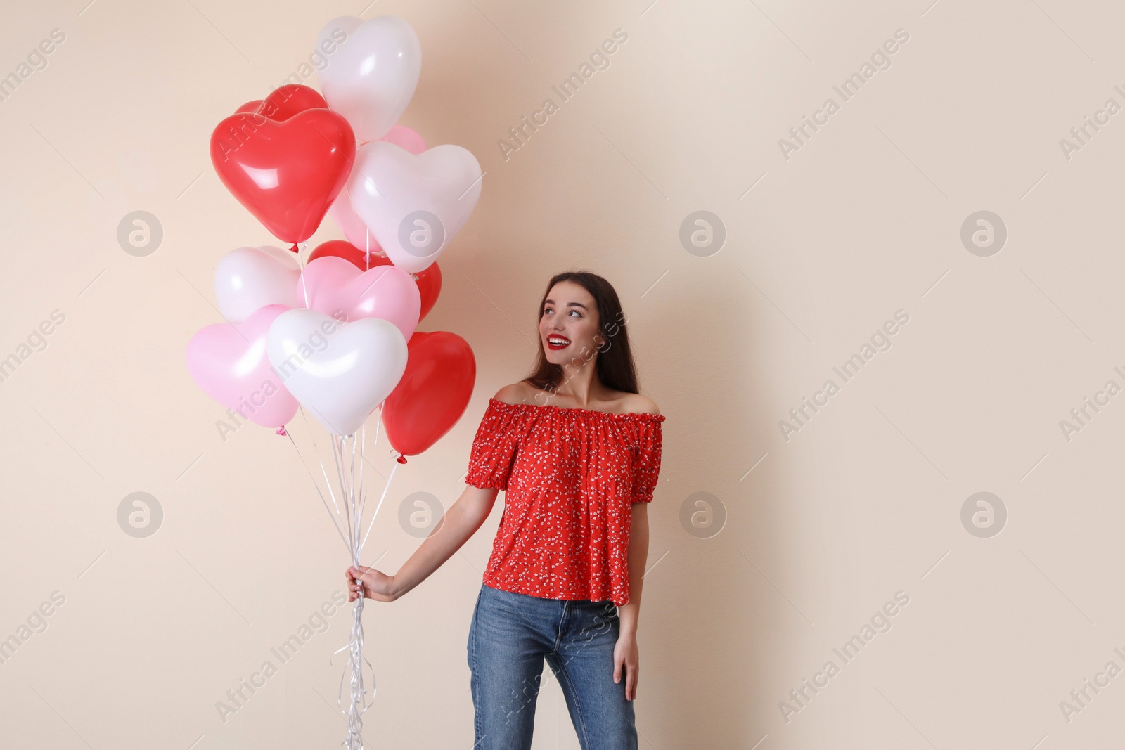 Photo of Beautiful young woman with heart shaped balloons on beige background. Valentine's day celebration