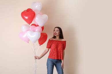 Beautiful young woman with heart shaped balloons on beige background. Valentine's day celebration