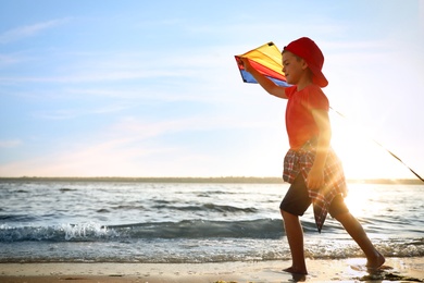 Photo of Cute little child with kite running on beach near sea at sunset. Spending time in nature