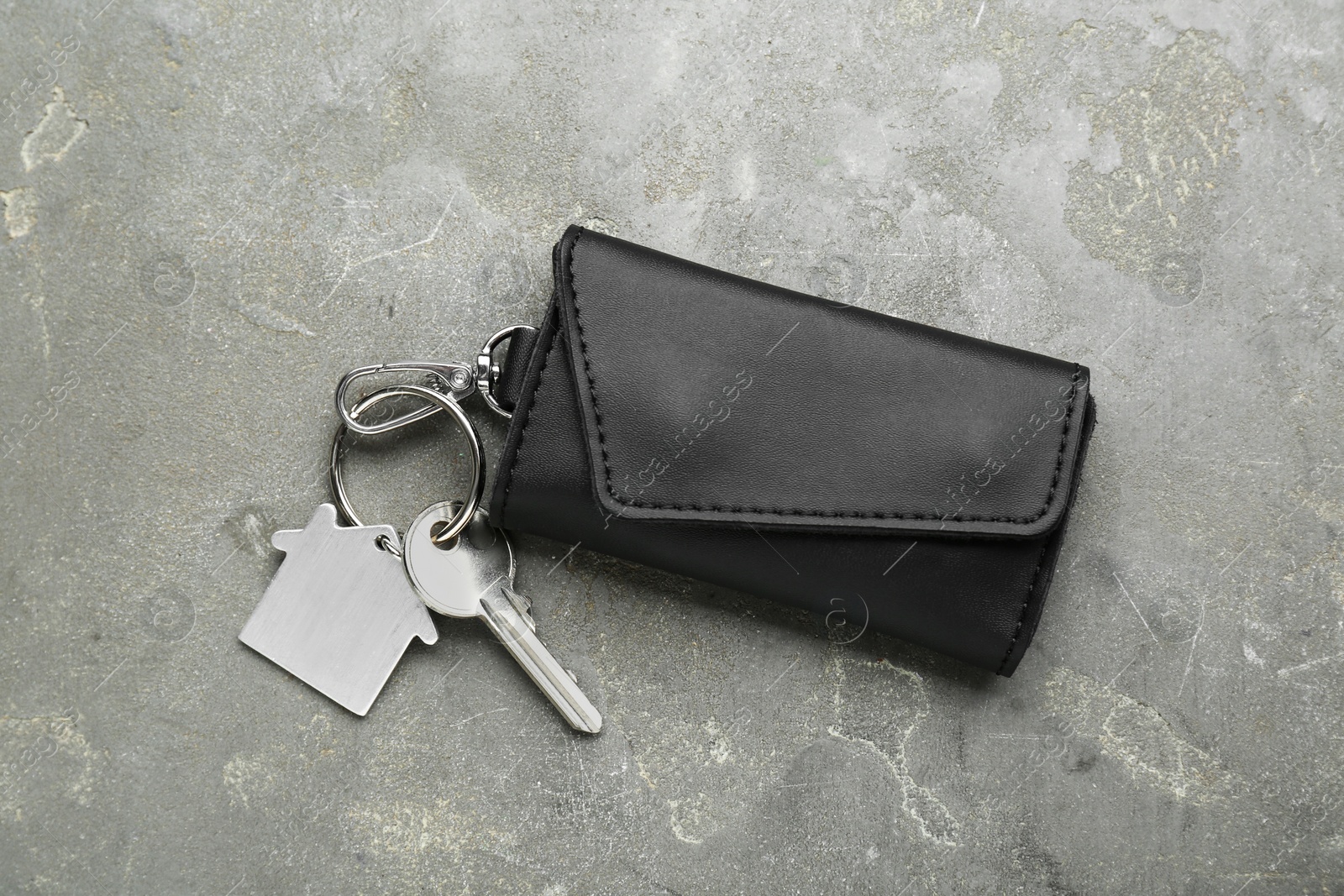 Photo of Leather case with key on grey textured table, top view.