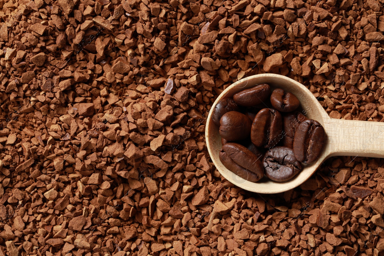 Photo of Spoon with roasted beans on instant coffee, top view