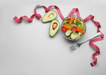 Measuring tape, salad, fork and halves of avocado on light background, flat lay. Space for text