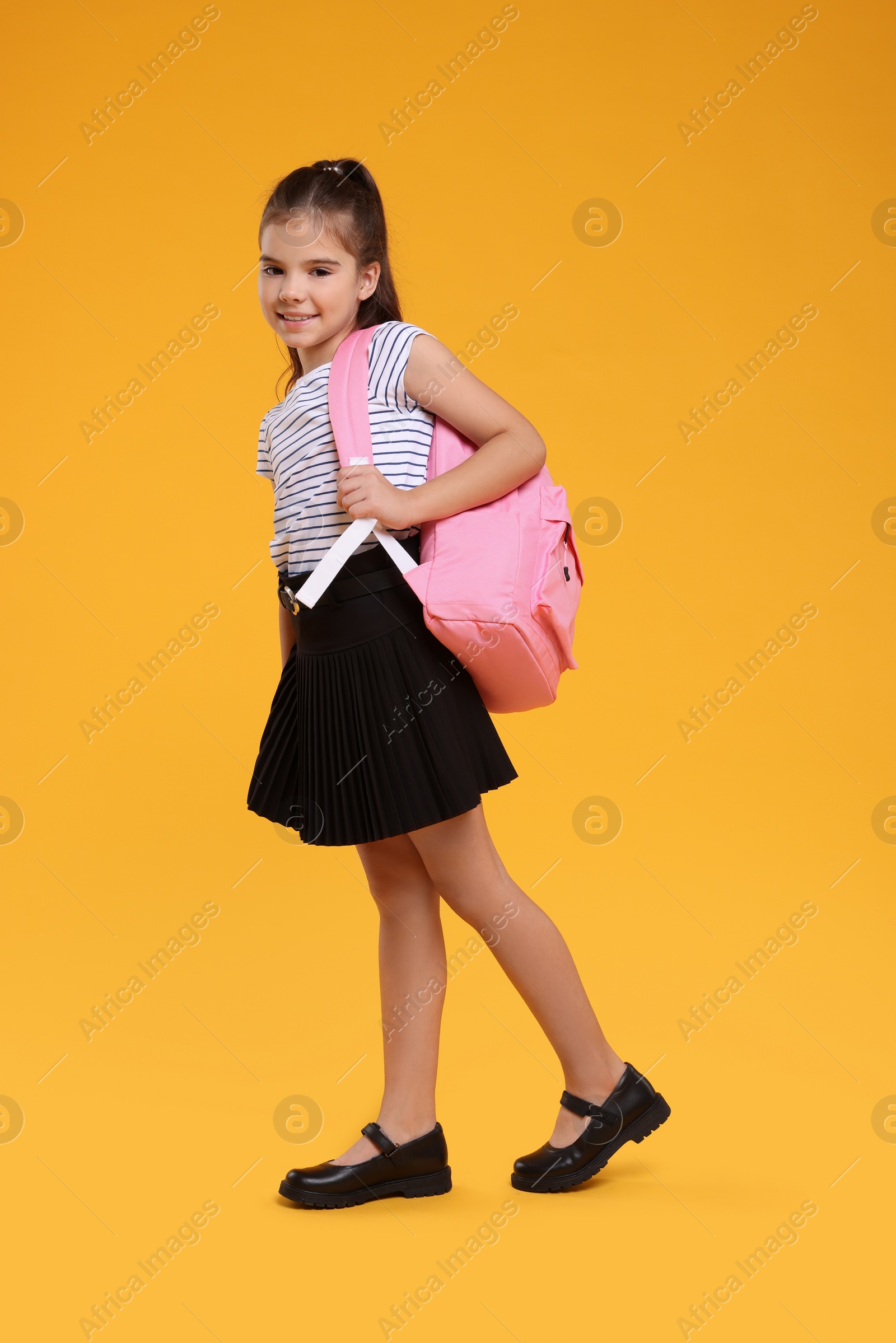 Photo of Back to school. Cute girl with backpack walking on orange background