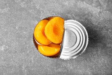 Photo of Tin can with conserved peaches on grey background, top view