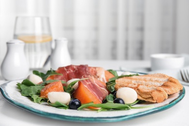 Photo of Fresh melon with prosciutto, mozzarella and arugula on white table