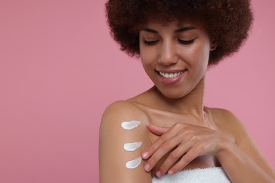 Photo of Beautiful young woman applying body cream onto arm on pink background, space for text
