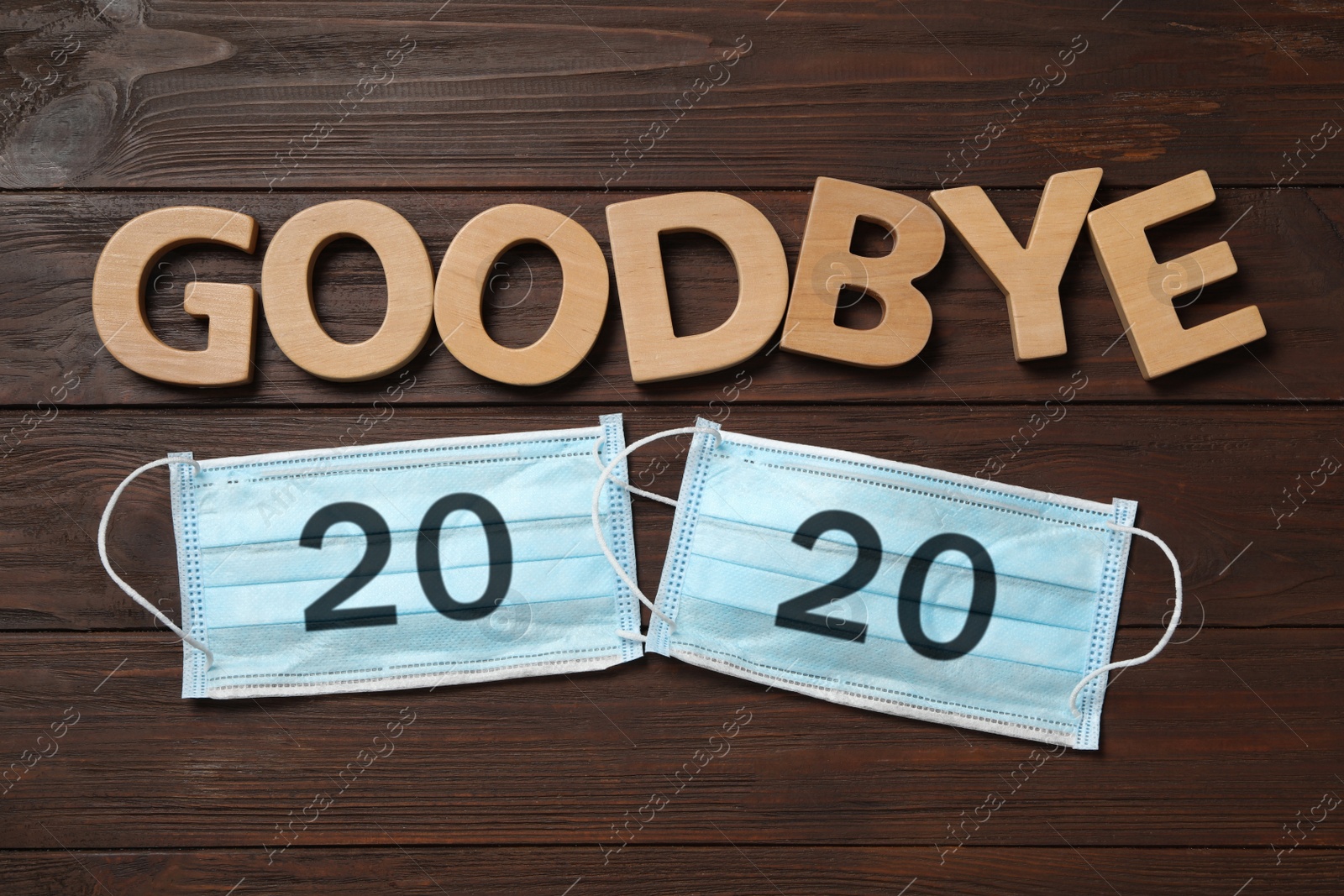 Photo of Text Goodbye 2020 and medical face masks on wooden background, flat lay