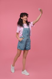 Beautiful young woman taking selfie on pink background