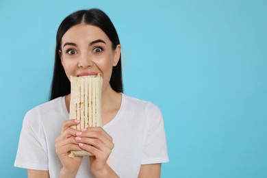 Photo of Young woman eating delicious shawarma on light blue background. Space for text