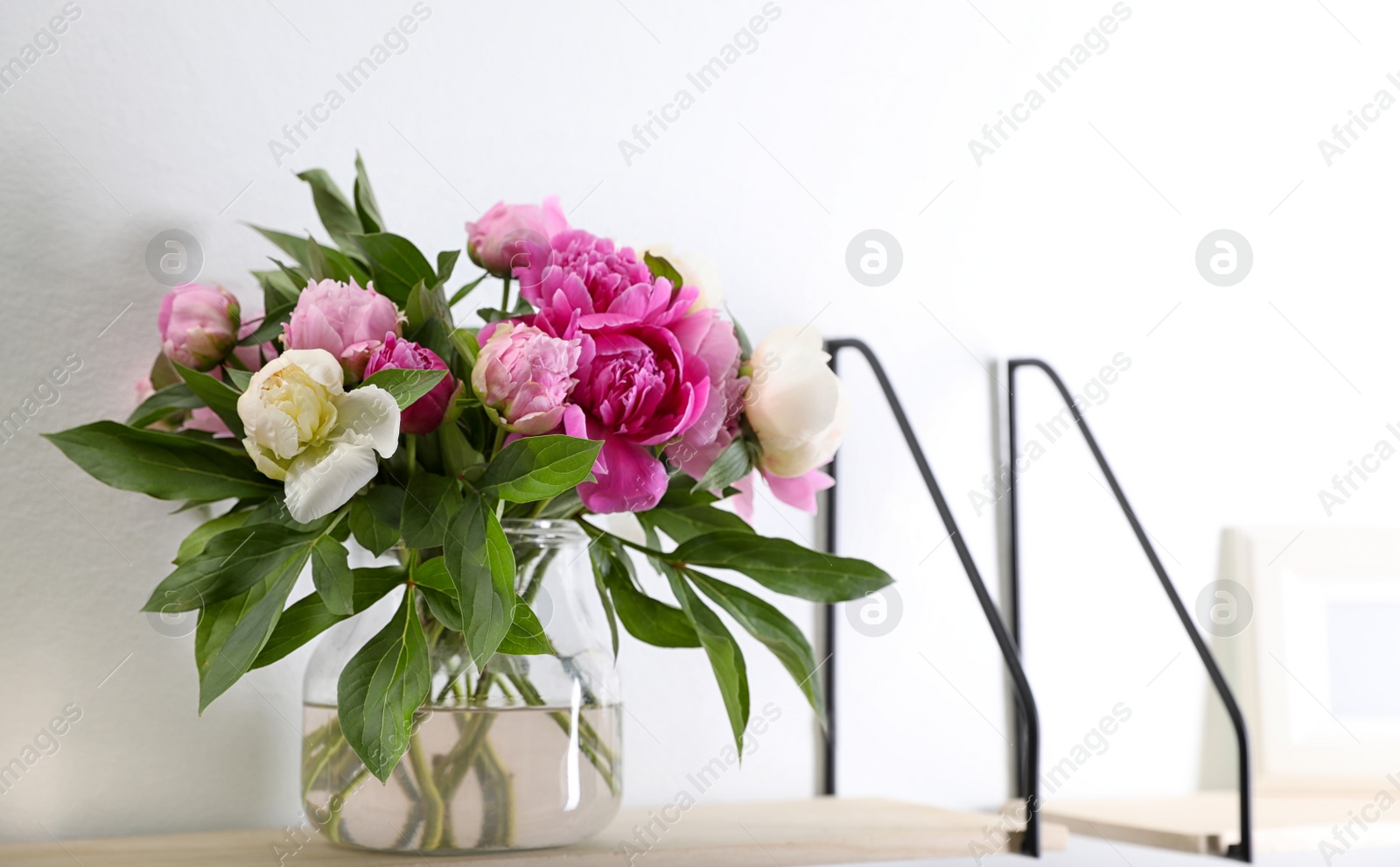 Photo of Shelf with vase of beautiful peonies on white wall. Space for text