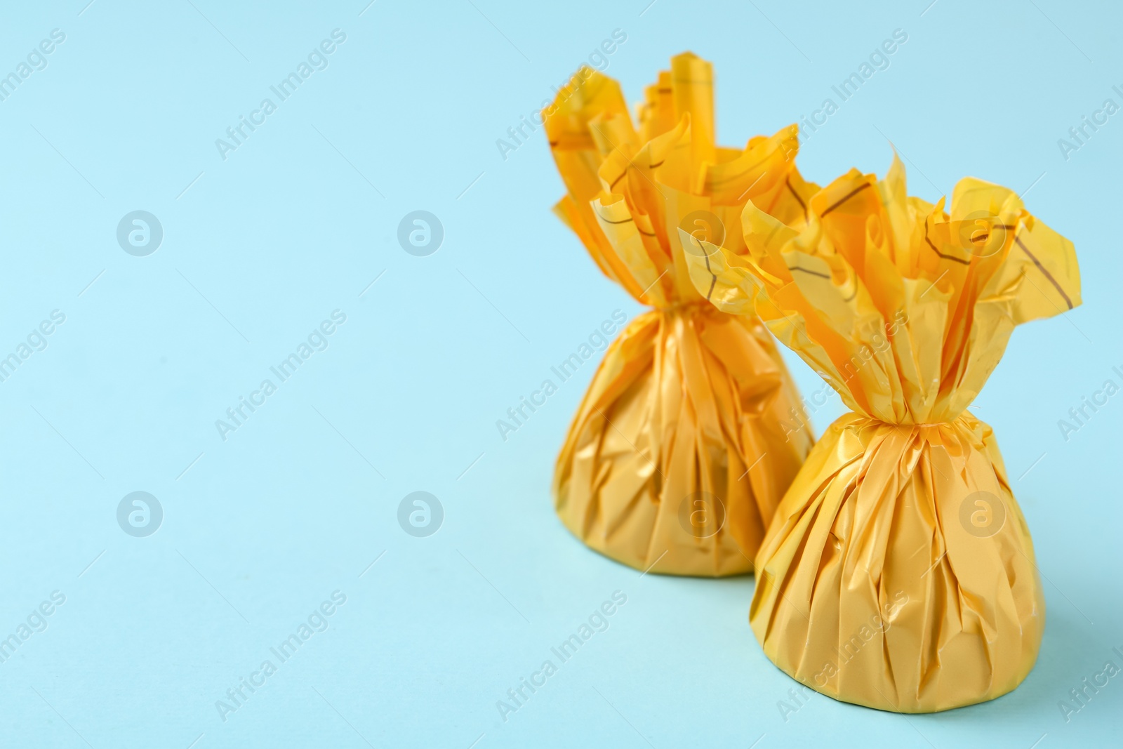 Photo of Candies in yellow wrappers on light blue background. Space for text