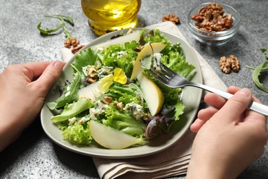 Photo of Woman eating fresh salad with pear at grey table, closeup