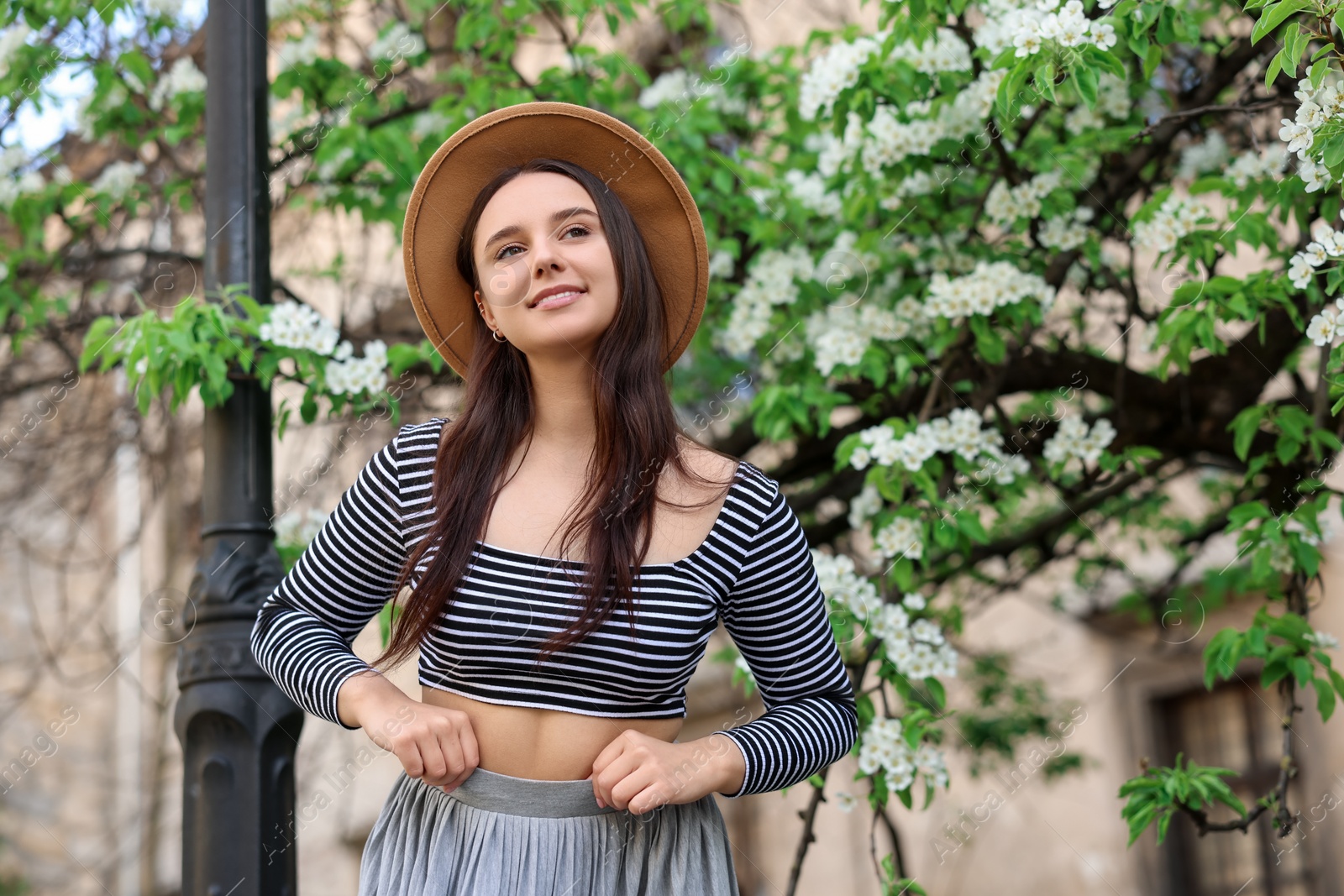 Photo of Beautiful woman in hat near blossoming tree on spring day