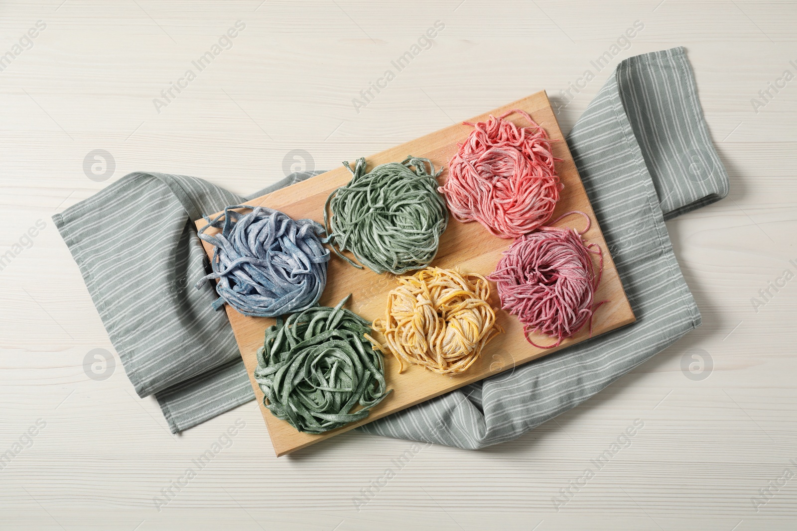 Photo of Rolled pasta painted with food colorings on white wooden table, top view