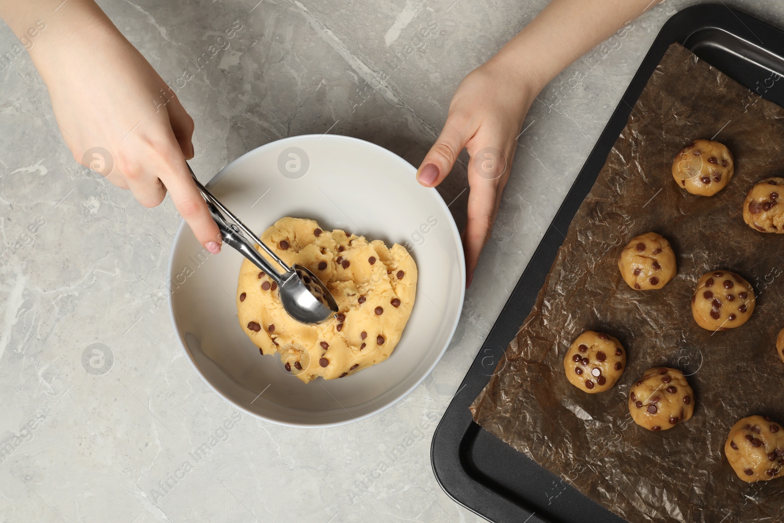 Photo of Woman making delicious chocolate chip cookies at light grey table, top view