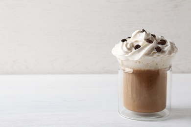 Glass cup of tasty coffee with whipped cream on wooden table. Space for text