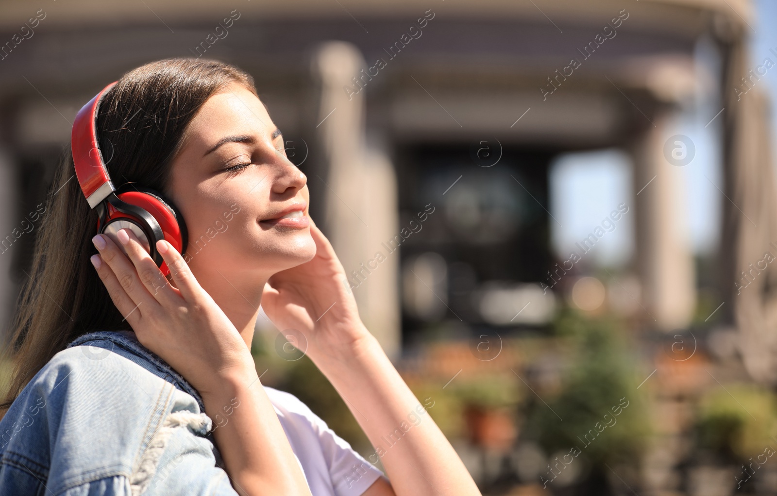 Photo of Young woman with headphones listening to music outdoors. Space for text